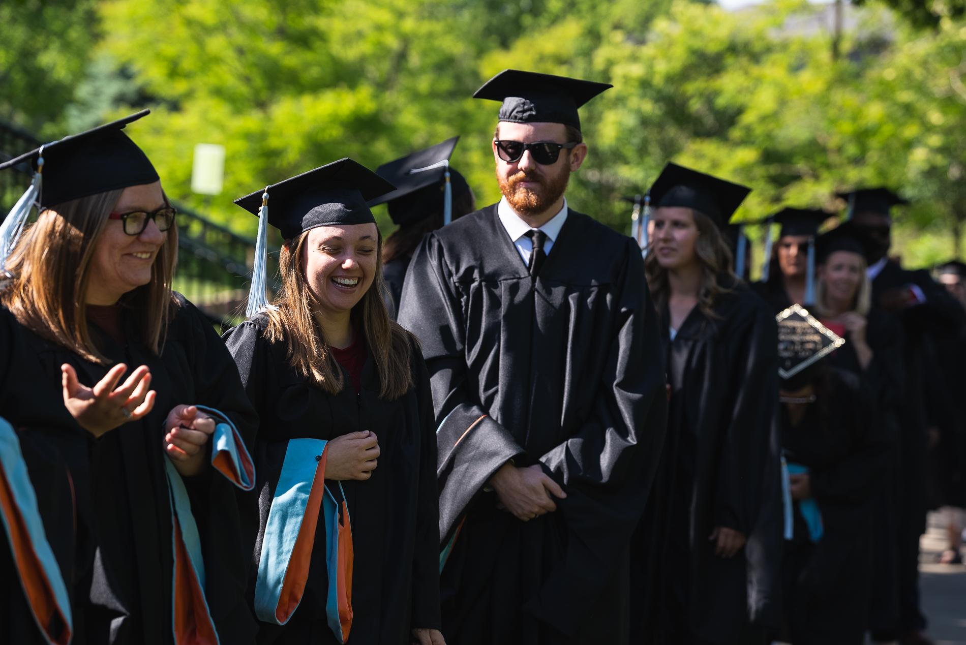 毕业生们身着黑色长袍，头戴黑色帽子, with blue tassels, 在排队参加毕业典礼时开怀大笑.