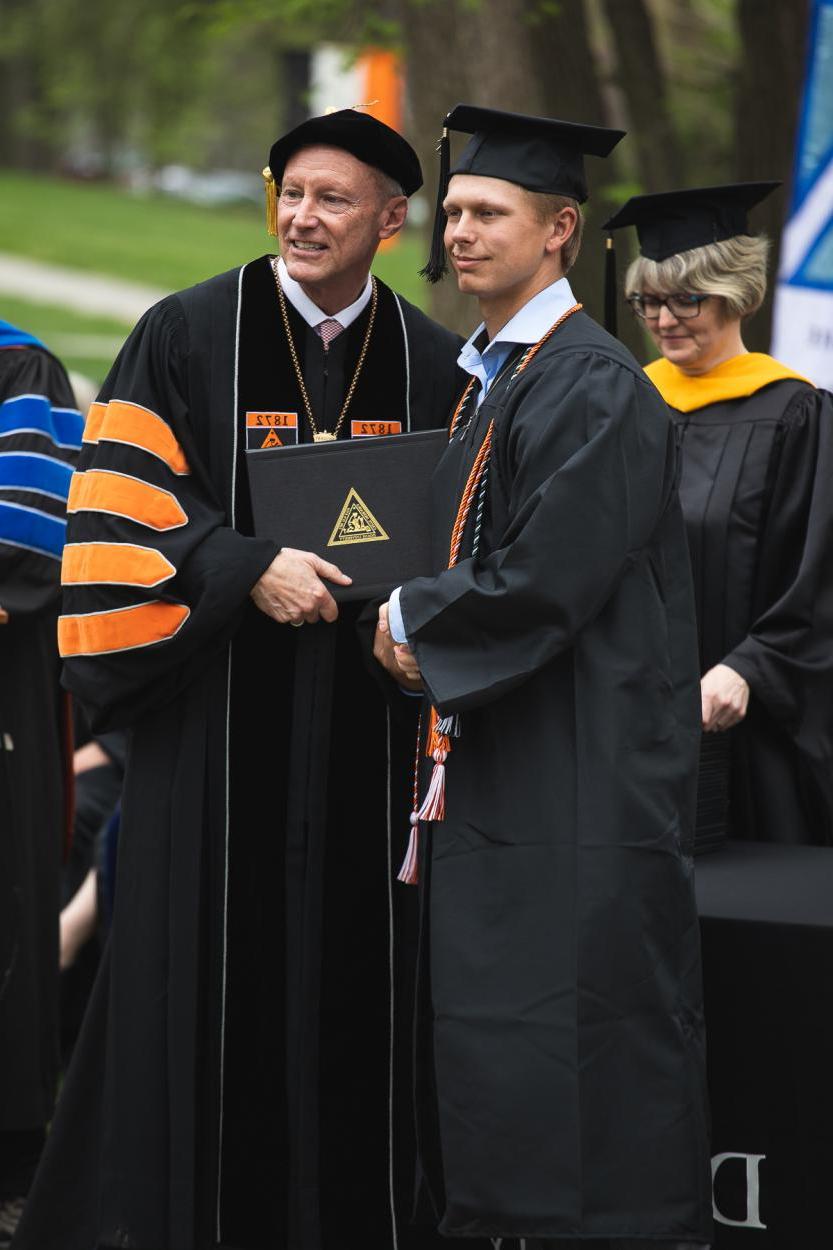 22岁的杰克逊·斯滕斯加德(Jackson Stensgard)拿着自己的毕业证书，在约翰逊博士(Dr. 罗杰·休斯在2022年5月8日的毕业典礼上. 