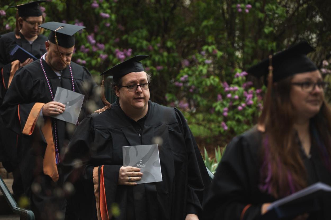 Patrick Neff '22B walks by one of Doane's Crete campus's flowering bushes during the commencement processional on May 8, 2022. 