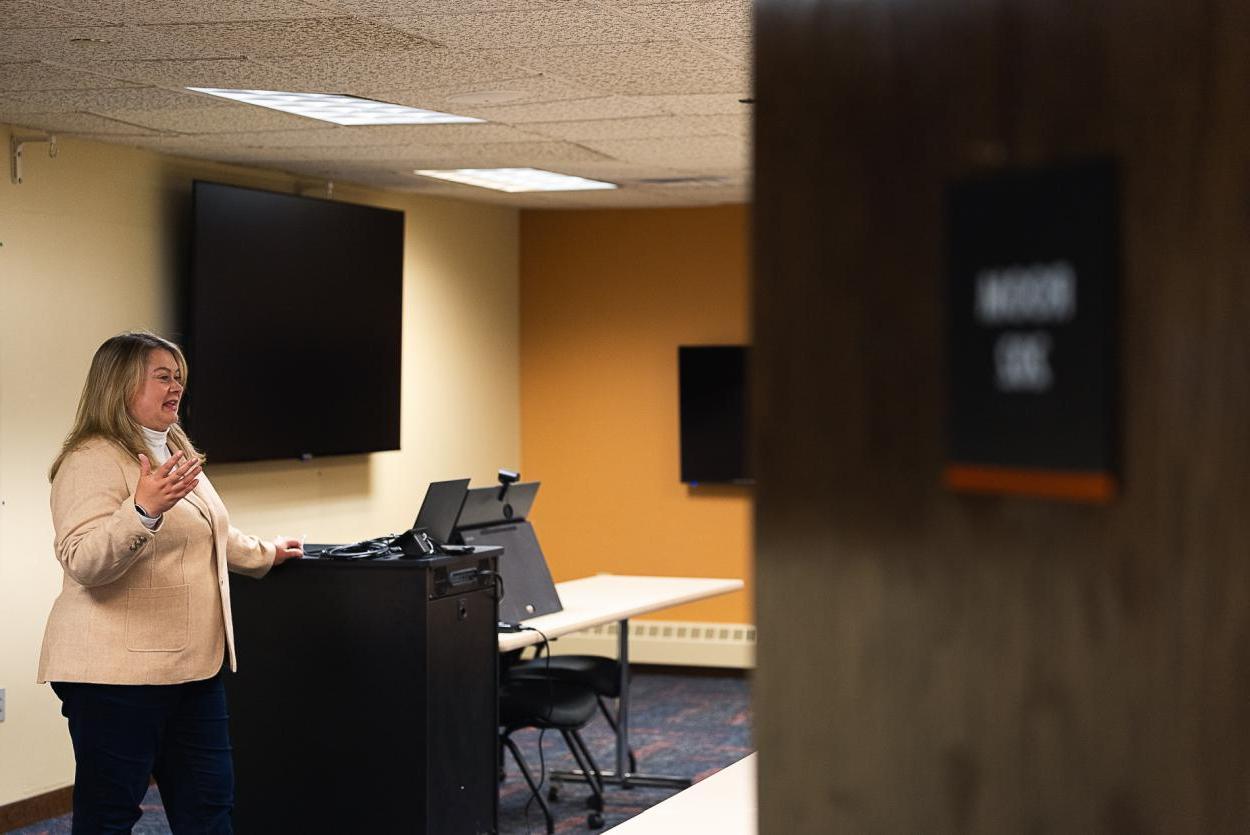 Dr. 詹妮弗·波萨德 speaks at the front of the 商学院's technology classroom, 位于林肯的弗雷德·布朗中心. 部分关闭的门覆盖了图像的一部分, 而在Bossard的后面是两台大电视, 一个平板电脑和一个附加技术的橱柜.