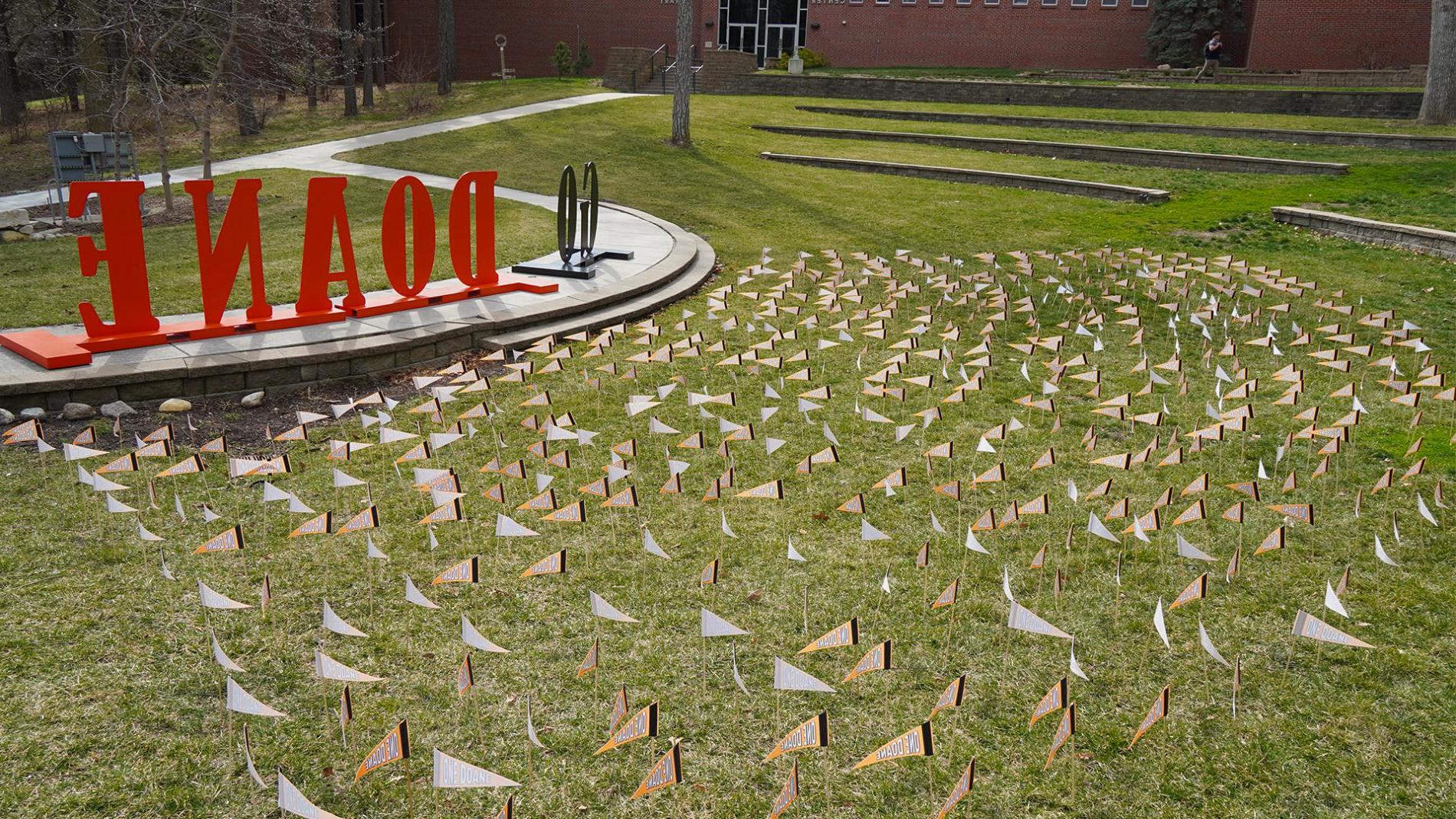 Cassel Outdoor Theatre on Doane’s 克里特岛 campus has nearly 700 orange pennants on display atop the green grass. Giant letters reading G-O D-O-A-N-E can be seen near the pennants. 